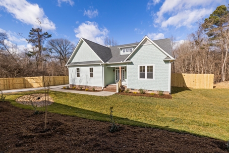A newly built home featuring a dark gray shingle roof, light green siding, a well-manicured lawn, and a wooden privacy fence, highlighting modern residential roofing and home exterior design.