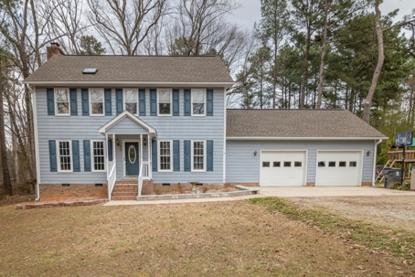 Suburban house in country side. Tan grass with pine trees in the background. The asphalt roof has a beautiful contrast against the light-blue exterior of two-door garaged house.
