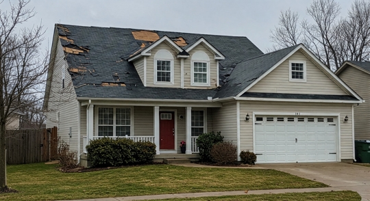 A suburban home with severe storm damage, missing shingles, and exposed roof decking, highlighting the risks of neglected roof maintenance and the importance of home insurance claims.