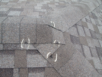 Close-up of a roof with chalk-marked storm damage on shingles, emphasizing the need for regular maintenance and inspections.